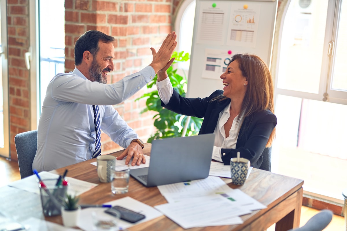 Two people high-fiving at a desk with a laptop